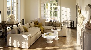 Sonnendurchflutetes Wohnzimmer mit großem beigem Sofa, Holzboden und großen Fenstern.