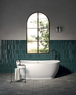 Weiße, freistehende Badewanne vor einer Wand mit grünen Fliesen und einem Bogenfenster.