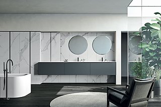 Großzügiges Badezimmer mit Marmorwand und einem langen, grauen Waschtisch mit zwei runden Spiegeln.