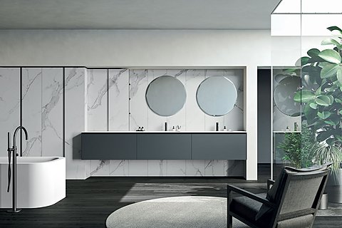 Großzügiges Badezimmer mit Marmorwand und einem langen, grauen Waschtisch mit zwei runden Spiegeln.