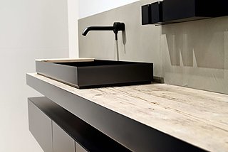 Nahaufnahme eines schwarzen, aufgesetzten Waschbeckens auf einer rustikalen Holzplatte.