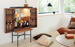 Ein offener, wandmontierter Barschrank aus Holz, gefüllt mit Flaschen und Gläsern.