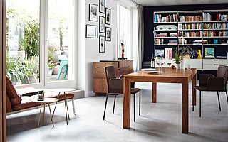 Ein Essbereich mit Holztisch und Lederstühlen vor einem großen Bücherregal.