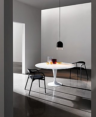 Ein runder, weißer Esstisch mit zwei schwarzen Stühlen in einem minimalistischen Raum.