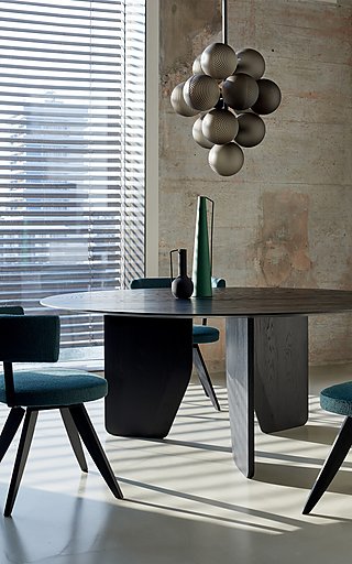 Ein runder, dunkler Holztisch mit blaugrünen Stühlen und einer modernen Lampe.