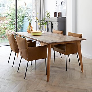 Ein rustikaler Holztisch mit vier braunen Lederstühlen auf einem Fischgrät-Parkettboden.