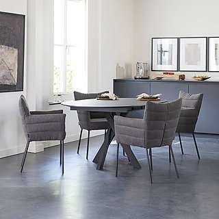 Ein runder, ausziehbarer, dunkelgrauer Esstisch mit passenden gepolsterten Stühlen.