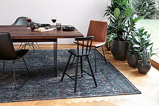 Ein gedeckter Esstisch aus dunklem Holz mit einem schwarzen Kinderhochstuhl auf einem gemusterten Teppich.