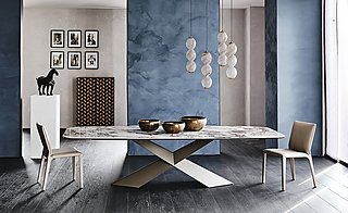 Ein langer Esstisch mit Marmorplatte und skulpturalem Metallfuß vor einer blauen Wand.