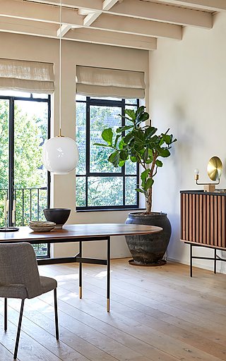 Ein ovaler Holztisch neben einer großen Pflanze und einem Sideboard mit geriffelten Türen.