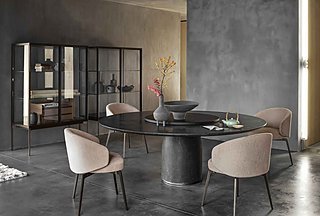 Ein runder, dunkler Steintisch mit beigen Stühlen vor einer grauen Wand und einer Glasvitrine.