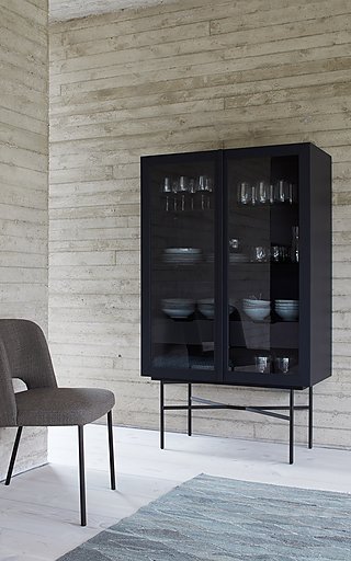 Eine schwarze Vitrine mit Glasfronten vor einer hellen Betonwand.