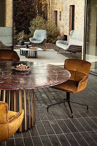 Ein runder Tisch mit roter Marmorplatte und einem senffarbenen Stuhl auf einer Terrasse.