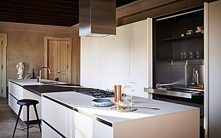 Eine minimalistische weiße Küche mit einer langen Insel und einer versteckten Arbeitsstation.