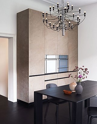 Ein deckenhoher, beiger Küchenschrank neben einem schwarzen Esstisch.