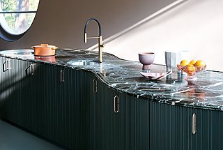 Nahaufnahme einer geschwungenen Kücheninsel mit grüner Marmorplatte und geriffelten Fronten.