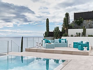 Eine türkisfarbene Sofagarnitur am Rande eines Pools mit Meerblick.