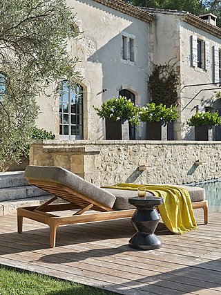 Eine hölzerne Sonnenliege mit gelbem Tuch neben einem Pool.