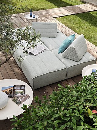 Ein modulares, hellgrünes Sofa auf einer Holzterrasse, umgeben von Pflanzen.