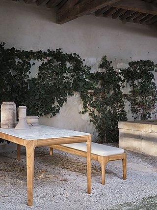 Ein Holztisch mit passender Bank an einer mit Efeu bewachsenen Wand.