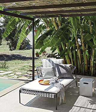 Eine Chaiselongue mit gestreiften Kissen unter einem Sonnenschutz am Pool.