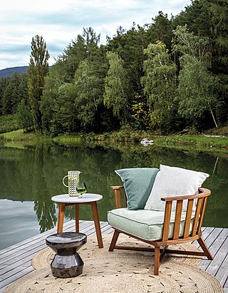 Ein Holzsessel mit Kissen auf einem Steg an einem See.