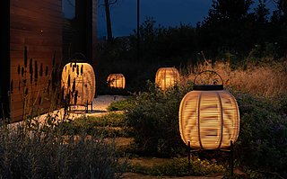 Drei geflochtene Laternen in einem Garten bei Nacht.