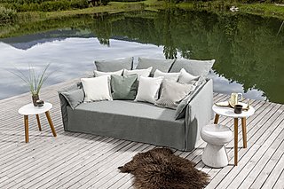 Ein graues Sofa mit vielen Kissen auf einem Holzsteg am See.