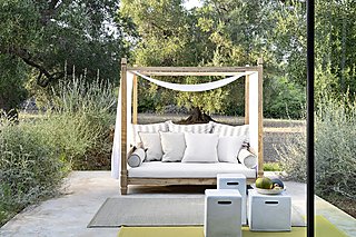 Ein Tagesbett aus Holz mit weißen Vorhängen auf einer Terrasse.