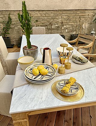 Ein gedeckter Marmortisch auf einer Holzterrasse mit einem Kaktus.