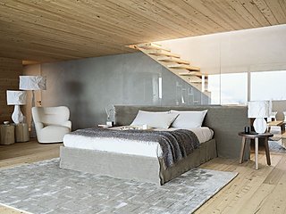 Ein graues Bett in einem modernen Schlafzimmer mit Holzdecke und Holztreppe.