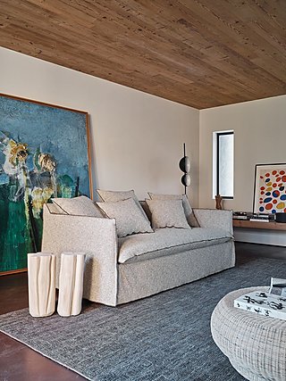 Ein beiges Sofa in einem Wohnzimmer mit Holzdecke und einem großen, bunten Gemälde.