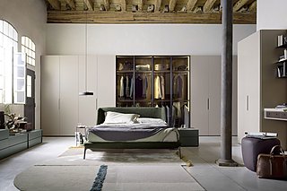 Ein grünes Bett in einem großen Raum mit einem begehbaren Kleiderschrank mit Glasfronten.