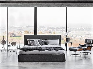 Ein dunkles Bett mit einem schwarzen Ledersessel in einem Raum mit Blick ins Grüne.