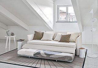 Ein hellbeiges Schlafsofa mit ausgezogener Liegefläche in einem Dachgeschosszimmer.