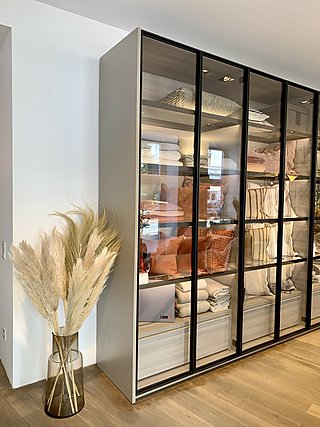 Ein moderner Kleiderschrank mit Glasfronten, in dem Kissen und Decken ordentlich gefaltet sind.