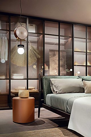 Ein Bett mit grünem Samt-Kopfteil vor einem Kleiderschrank mit Glasfronten.