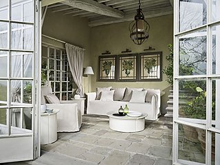 Ein heller Wintergarten mit einem weißen Sofa und Blick durch große Fenstertüren.