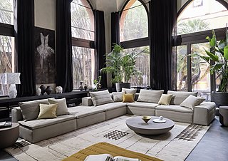 Eine große, modulare Couch in einem Raum mit hohen Bogenfenstern und einigen Pflanzen.