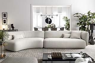 Ein geschwungenes, weißes Sofa in einem minimalistischen Wohnzimmer mit Essbereich im Hintergrund.