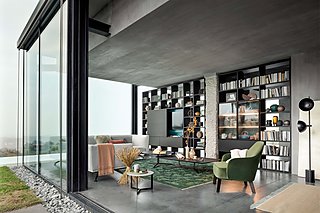 Ein modernes Wohnzimmer mit einem großen, schwarzen Bücherregal und einem grünen Sessel.