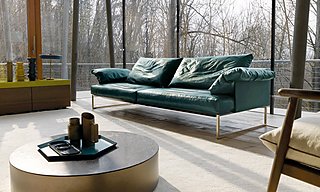 Ein petrolfarbenes Ledersofa in einem lichtdurchfluteten Raum mit Blick auf einen Wald.