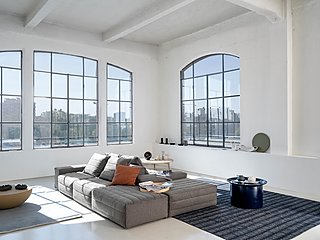 Ein graues, modulares Sofa in einem Loft-artigen Raum mit großen Fabrikfenstern.