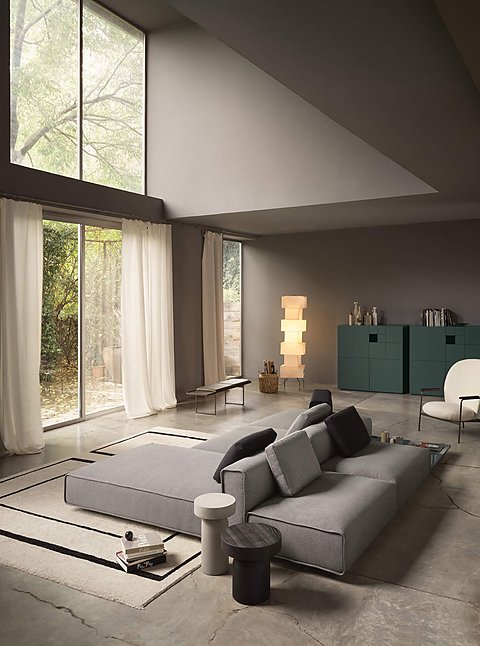 Eine große, graue Wohnlandschaft in einem modernen Raum mit Betonboden und Blick in den Garten.