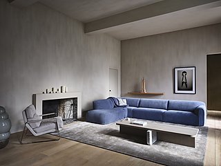 Ein großes, blaues Ecksofa in einem minimalistischen Raum mit Kamin.
