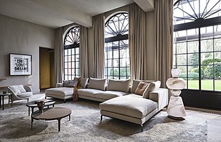 Eine große, helle Couch in einem eleganten Raum mit hohen Bogenfenstern und Blick in den Garten.