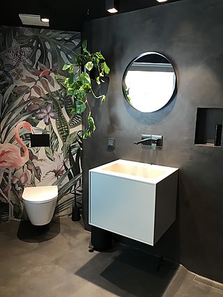 Dunkles Badezimmer mit tropischer Tapete, rundem Spiegel und weißem Waschtisch.