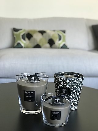 Duftkerzen von Baobab auf dem Couchtisch vor einem hellen Sofa mit gemustertem Kissen.