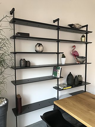 Schwarzes Metallwandregal mit Vasen, Keramik und dekorativen Objekten über dem Esstisch.