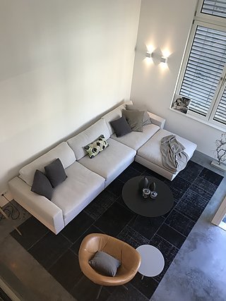 Wohnzimmer von der Galerie aus mit weißem Ecksofa, Lederfauteuil und dunklem Teppich.